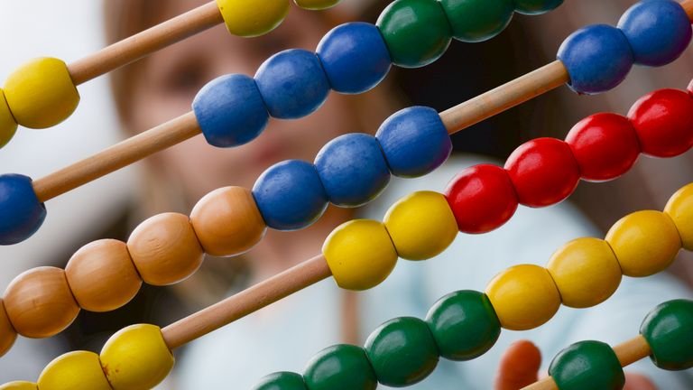 A child counting on a colourful abacus beside a maths worksheet