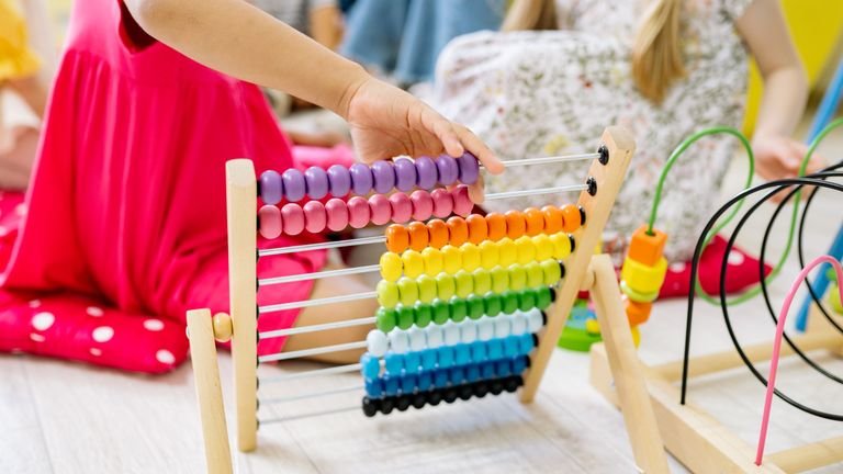 A girl holding up a wooden abacus with coloured beads