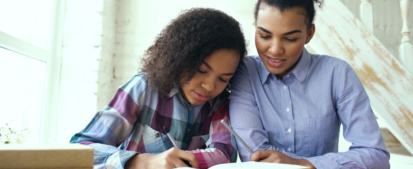 A parent helping a child with schoolwork at a table by a window