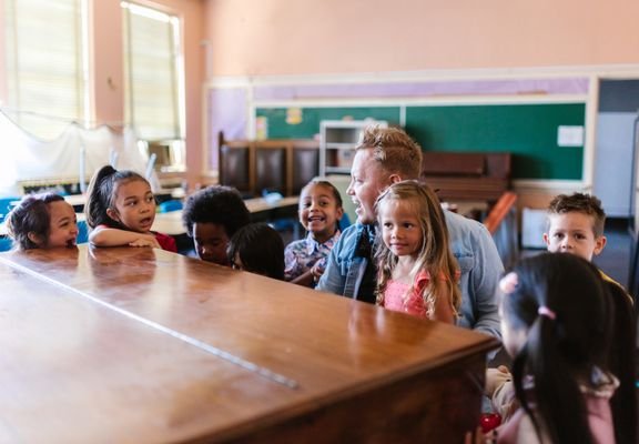 A teacher sitting with a group of young children around a large table.